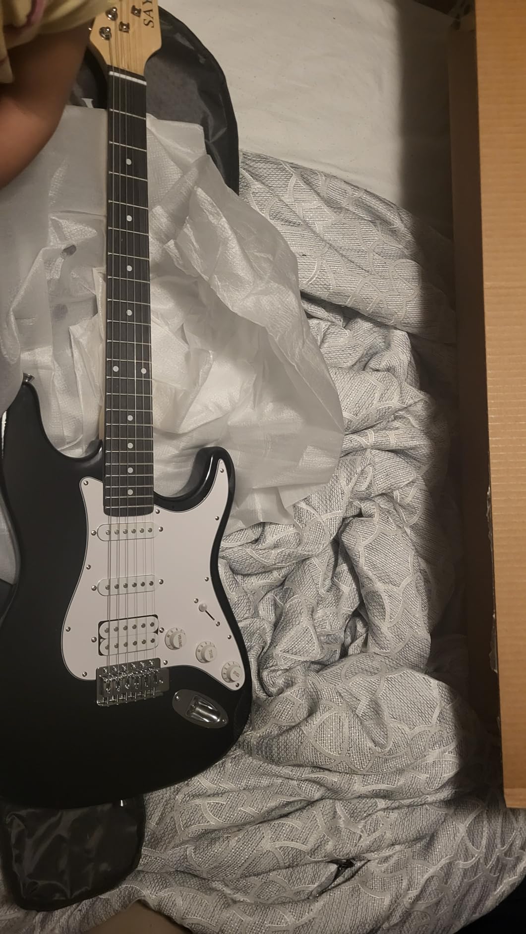 Black Sayha electric guitar just unpacked, lying on its plastic wrap