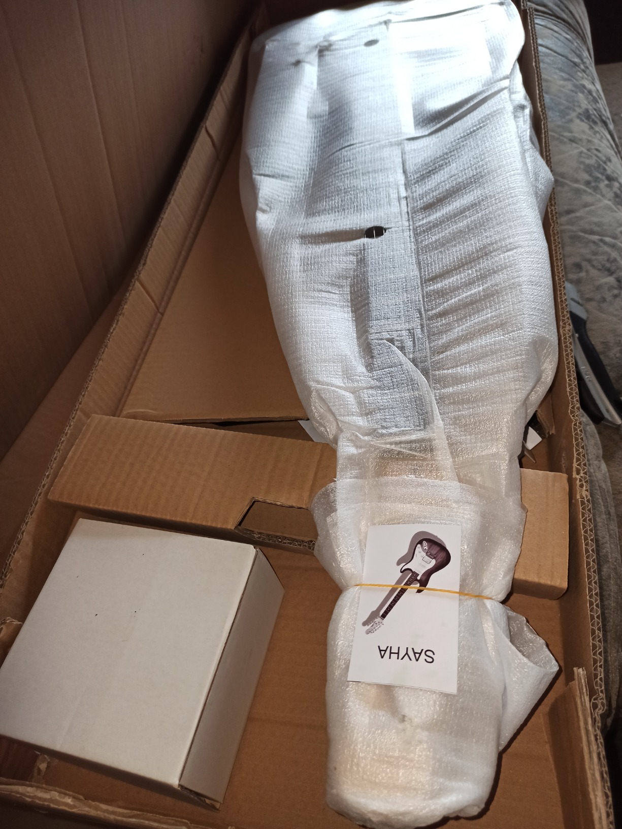 Sayha guitar wrapped in foam inside its shipping box, with the accessory box beside it