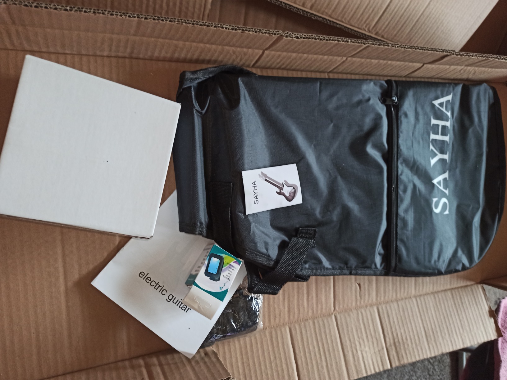 Opened Sayha shipping box with the gig bag, accessory box, clip-on tuner and manual